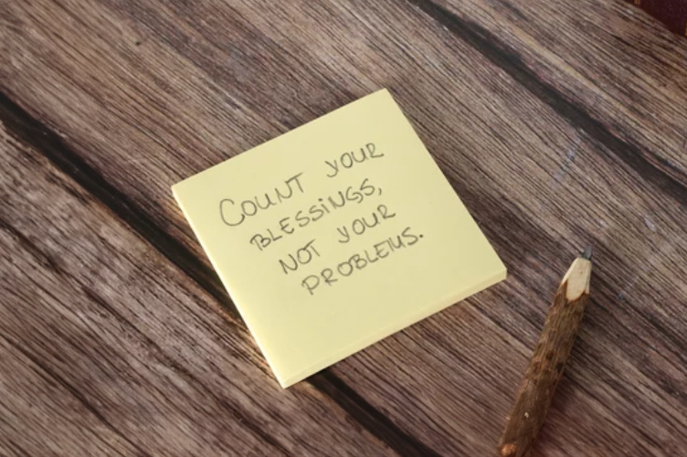 Inspirational quote on a sticky note reminding people to focus on their blessings rather than their problems.