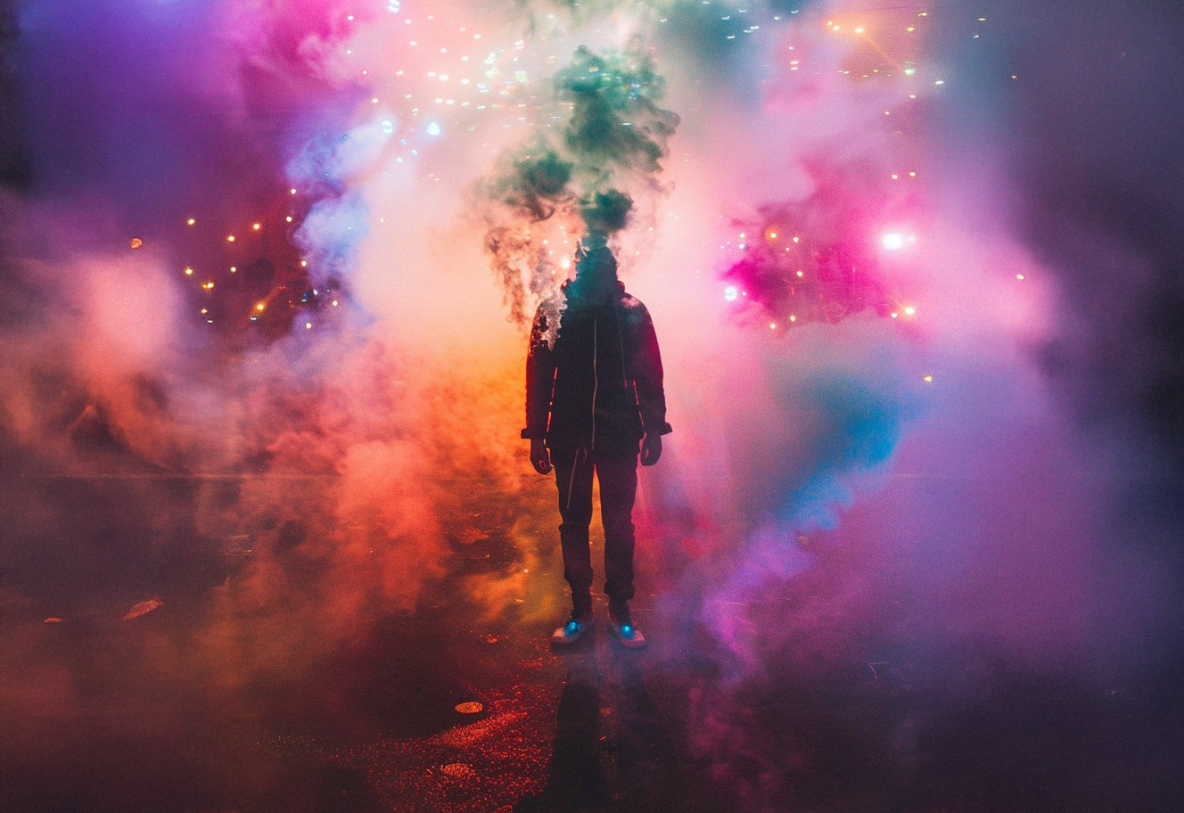 A person standing in a cloud of colourful smoke with a neon light background.